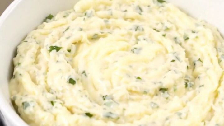 A glossy, creamy white cheddar dip in a white bowl with fresh herbs.