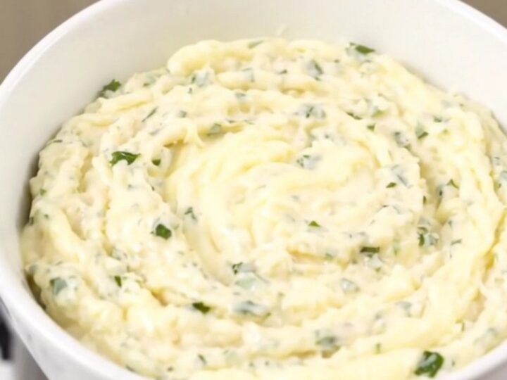 A glossy, creamy white cheddar dip in a white bowl with fresh herbs.