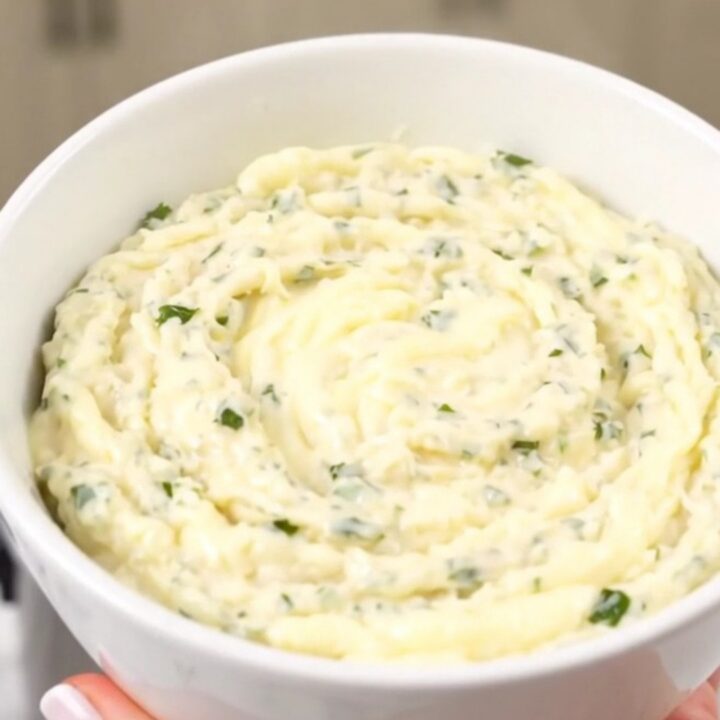 A glossy, creamy white cheddar dip in a white bowl with fresh herbs.