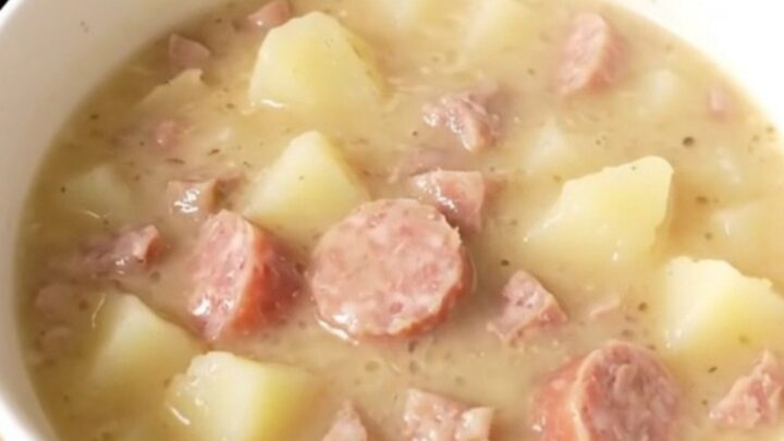 A steaming bowl of creamy white cheddar sausage chowder with visible pieces of sausage and potatoes.