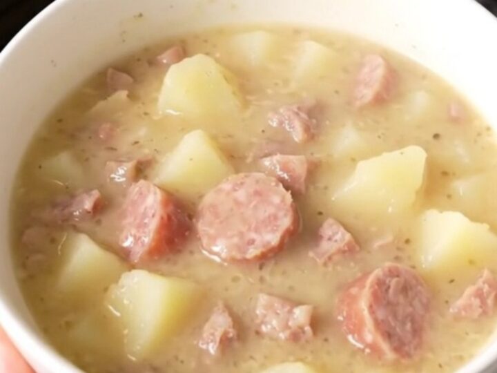 A steaming bowl of creamy white cheddar sausage chowder with visible pieces of sausage and potatoes.
