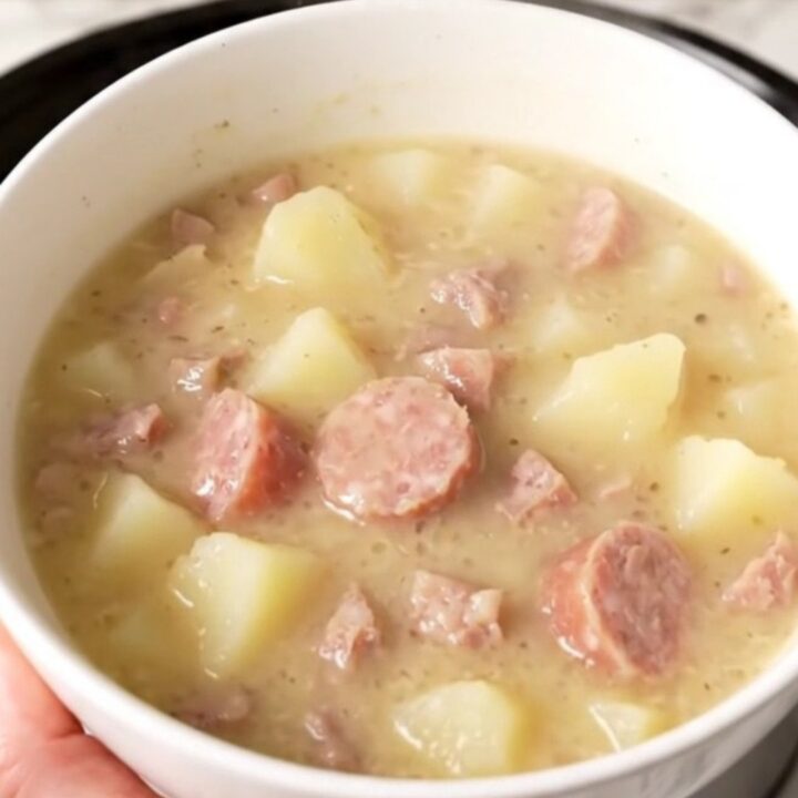 A steaming bowl of creamy white cheddar sausage chowder with visible pieces of sausage and potatoes.
