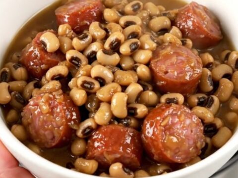 A top-down view of a slow cooker filled with sliced smoked sausage, black-eyed peas, and savory broth.