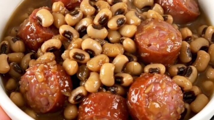 A top-down view of a slow cooker filled with sliced smoked sausage, black-eyed peas, and savory broth.