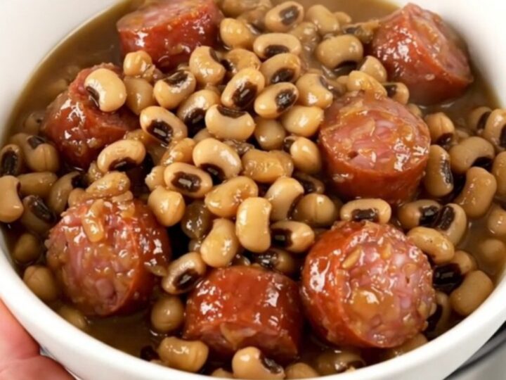 A top-down view of a slow cooker filled with sliced smoked sausage, black-eyed peas, and savory broth.