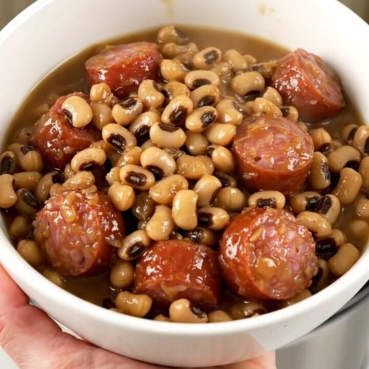 A top-down view of a slow cooker filled with sliced smoked sausage, black-eyed peas, and savory broth.