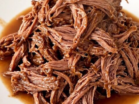 A close-up of a slow cooker filled with tender shredded beef and colorful giardiniera vegetables.