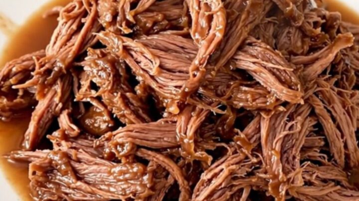 A close-up of a slow cooker filled with tender shredded beef and colorful giardiniera vegetables.