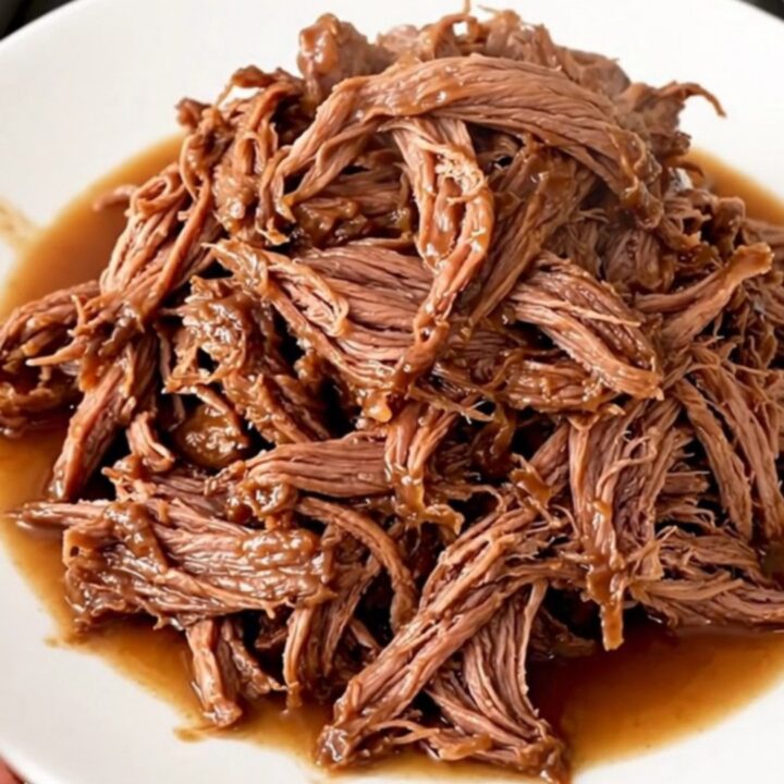 A close-up of a slow cooker filled with tender shredded beef and colorful giardiniera vegetables.
