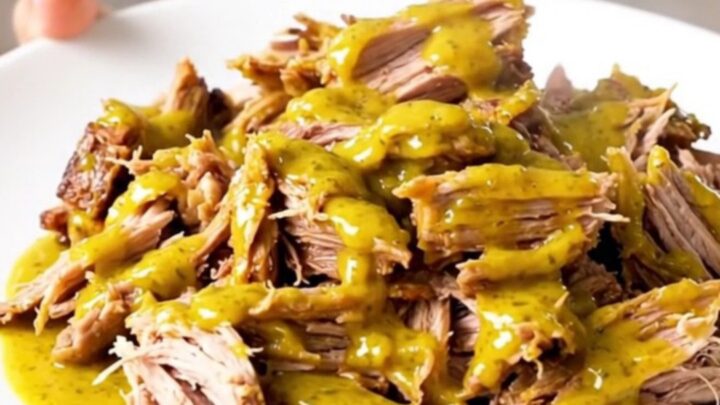 A close-up of tender, shredded Carolina mustard pulled pork on a white plate.