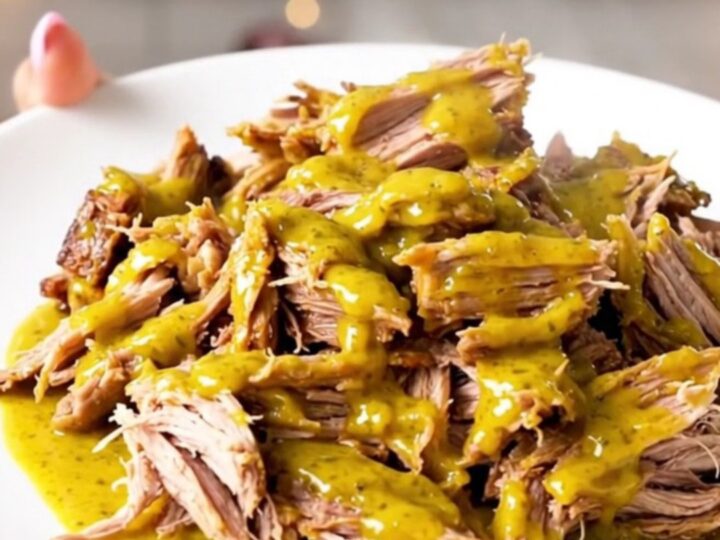 A close-up of tender, shredded Carolina mustard pulled pork on a white plate.