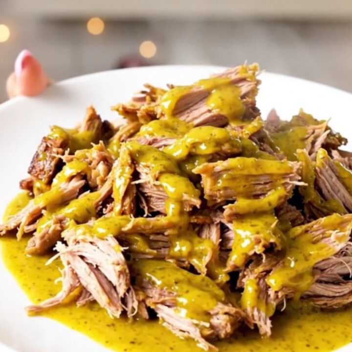 A close-up of tender, shredded Carolina mustard pulled pork on a white plate.