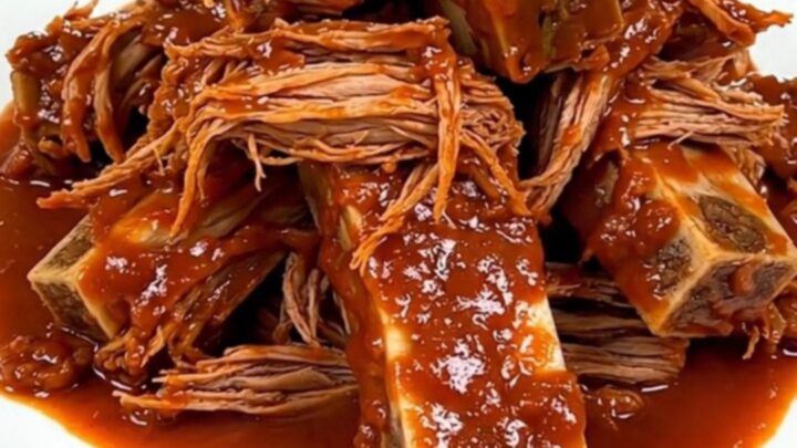 A close-up of tender, shredded Mexican braised short ribs in a glossy tomato sauce on a white plate.