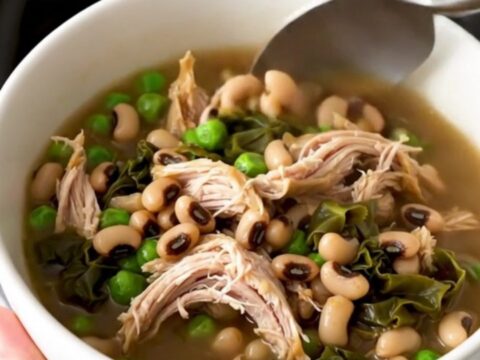 A black slow cooker filled with a hearty stew of shredded chicken, black-eyed peas, and collard greens.