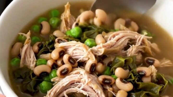 A black slow cooker filled with a hearty stew of shredded chicken, black-eyed peas, and collard greens.