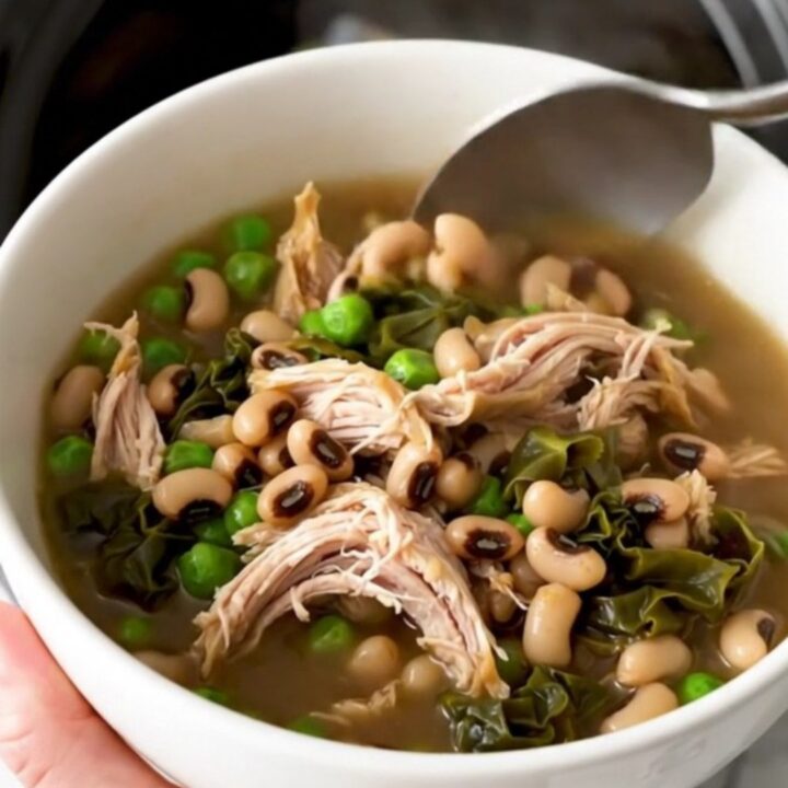 A black slow cooker filled with a hearty stew of shredded chicken, black-eyed peas, and collard greens.