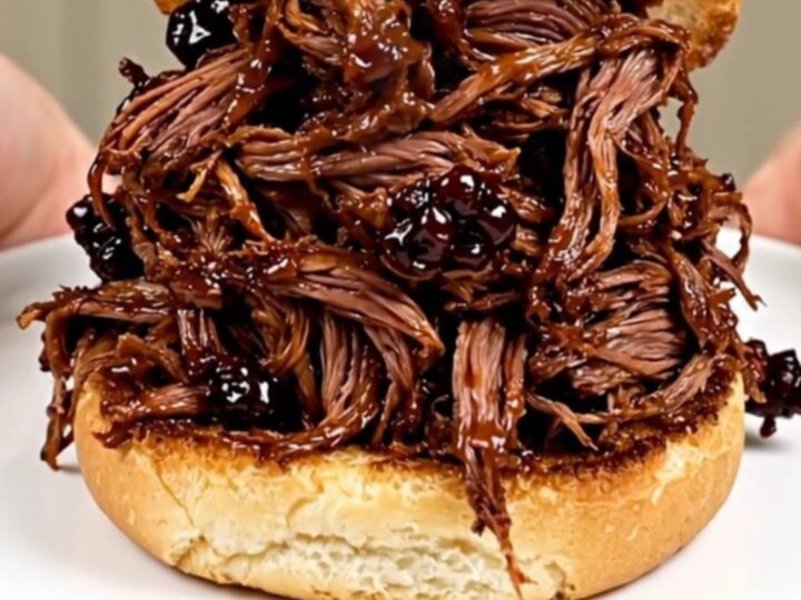 A close-up of glossy blackberry barbecue shredded beef piled high on a golden brioche bun.