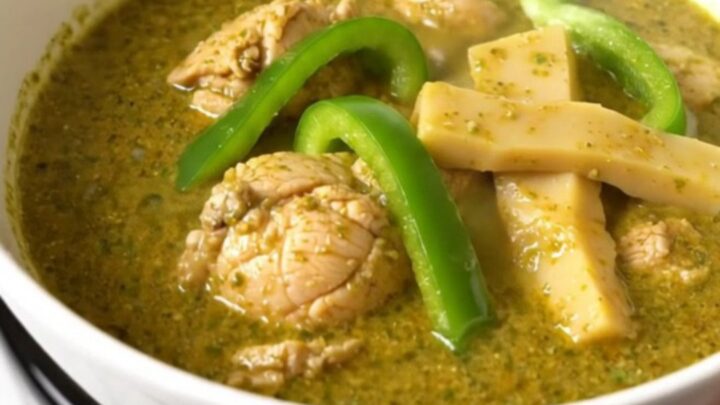 A top-down view of raw chicken, green peppers, and coconut milk in a black slow cooker on a white quartz countertop.