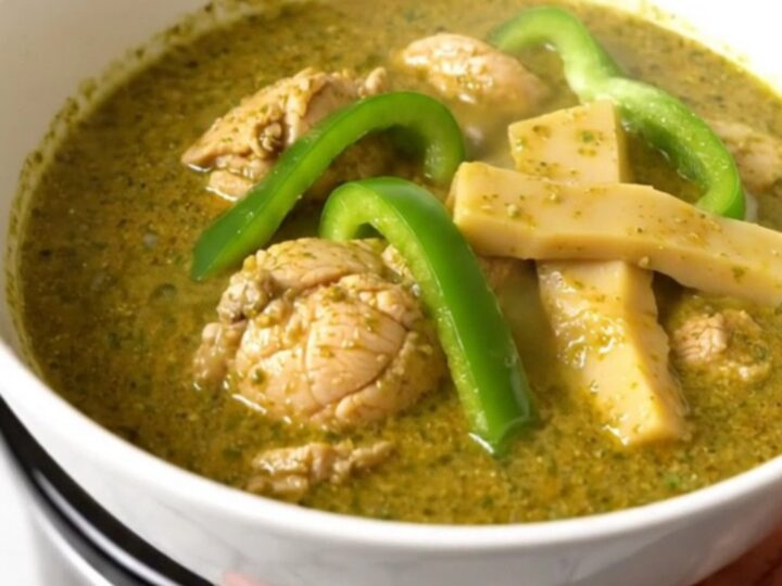 A top-down view of raw chicken, green peppers, and coconut milk in a black slow cooker on a white quartz countertop.