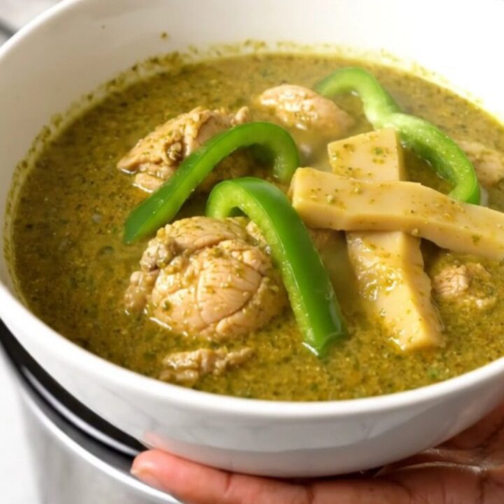 A top-down view of raw chicken, green peppers, and coconut milk in a black slow cooker on a white quartz countertop.