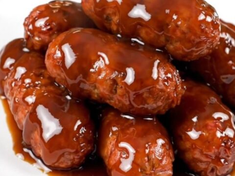 A top-down view of cooked Italian sausage bites in a honey-soy glaze inside a black slow cooker.