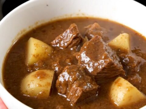 A close-up of a steaming bowl of beef stew with chunks of beef, potatoes, and green beans.