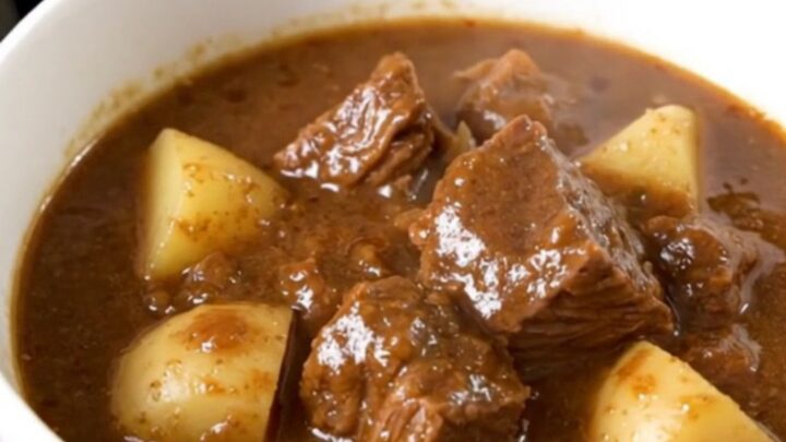 A close-up of a steaming bowl of beef stew with chunks of beef, potatoes, and green beans.