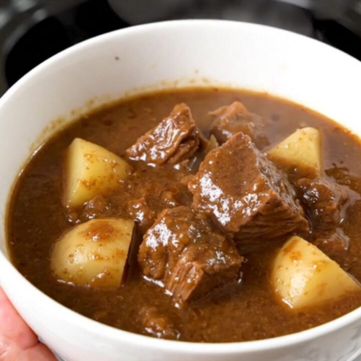 A close-up of a steaming bowl of beef stew with chunks of beef, potatoes, and green beans.