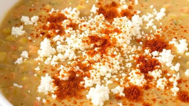 A white bowl filled with creamy Mexican street corn soup garnished with cotija cheese and chili powder.