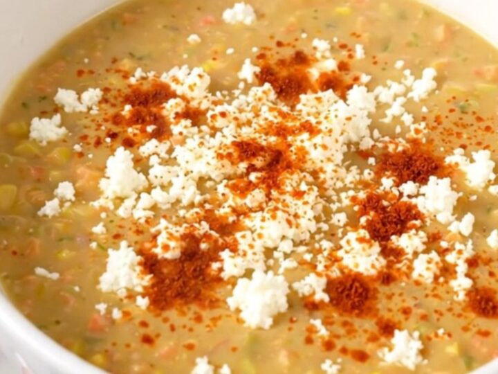 A white bowl filled with creamy Mexican street corn soup garnished with cotija cheese and chili powder.
