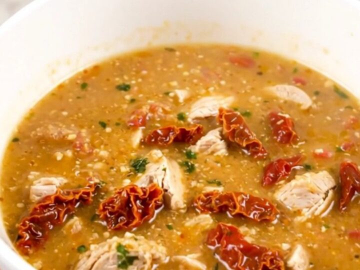 A steaming bowl of creamy chicken chowder with visible pieces of chicken, potatoes, and sun-dried tomatoes.