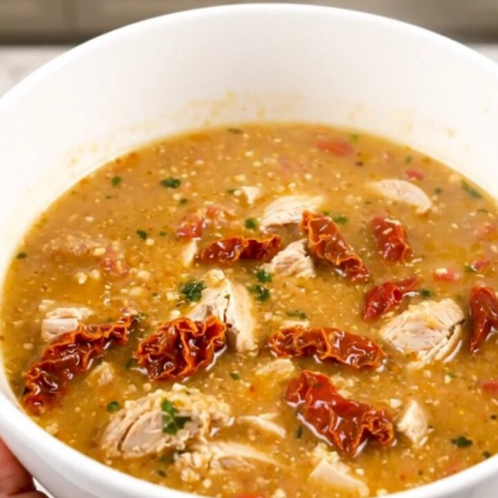 A steaming bowl of creamy chicken chowder with visible pieces of chicken, potatoes, and sun-dried tomatoes.