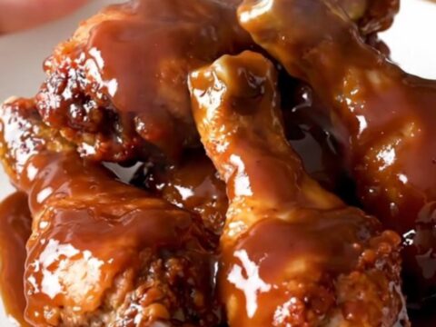 A close-up of glossy, slow-cooked chicken drumsticks covered in a rich barbecue glaze on a white plate.