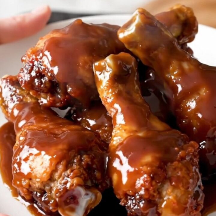 A close-up of glossy, slow-cooked chicken drumsticks covered in a rich barbecue glaze on a white plate.