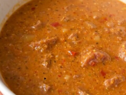 A steaming bowl of creamy sausage and roasted red pepper chowder served in a white bowl.