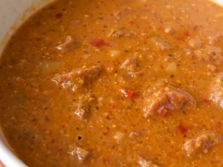 A steaming bowl of creamy sausage and roasted red pepper chowder served in a white bowl.