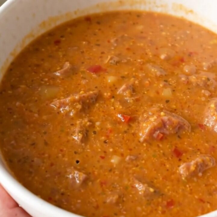 A steaming bowl of creamy sausage and roasted red pepper chowder served in a white bowl.
