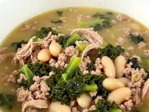 A steaming bowl of slow cooker ground turkey and white bean soup with kale, served in a white bowl.