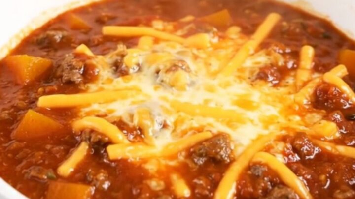 A white bowl filled with glossy beef and butternut squash chili topped with shredded cheese.