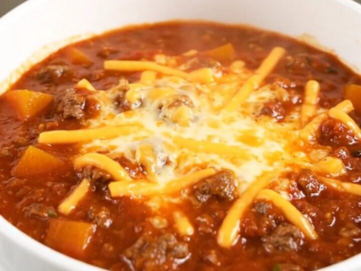 A white bowl filled with glossy beef and butternut squash chili topped with shredded cheese.