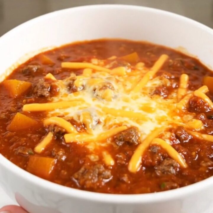 A white bowl filled with glossy beef and butternut squash chili topped with shredded cheese.