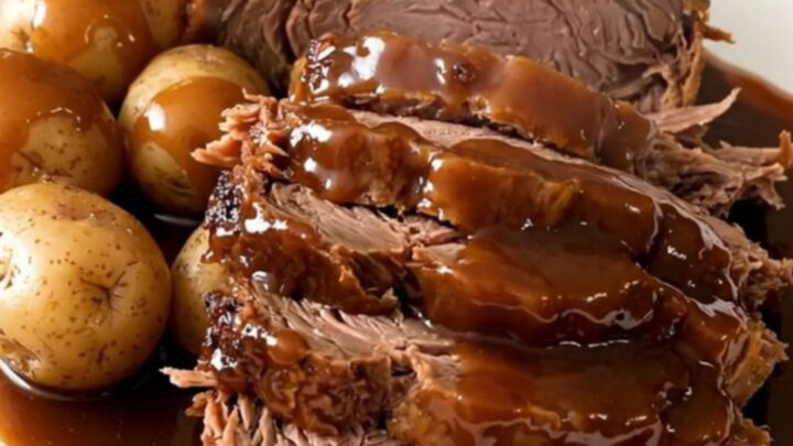 A slow cooker filled with a beef chuck roast, halved potatoes, and a dark, glossy molasses glaze.
