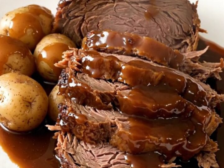 A slow cooker filled with a beef chuck roast, halved potatoes, and a dark, glossy molasses glaze.