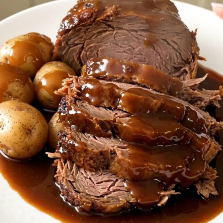 A slow cooker filled with a beef chuck roast, halved potatoes, and a dark, glossy molasses glaze.