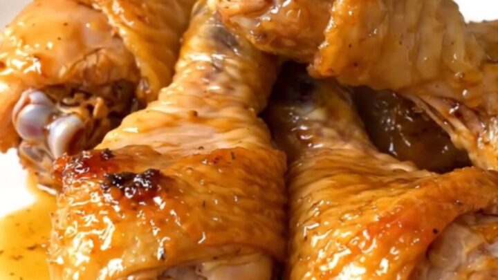 Golden, glossy crockpot garlic herb parmesan chicken drumsticks on a white plate.