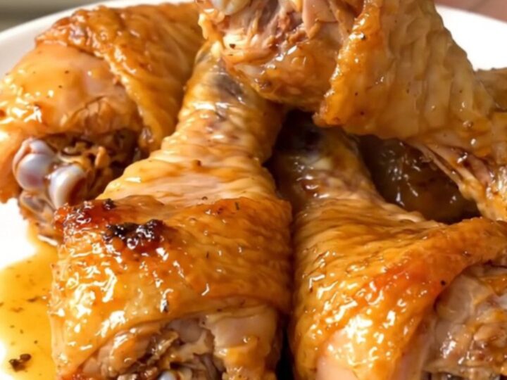 Golden, glossy crockpot garlic herb parmesan chicken drumsticks on a white plate.