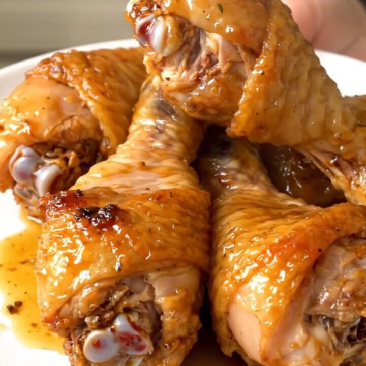 Golden, glossy crockpot garlic herb parmesan chicken drumsticks on a white plate.