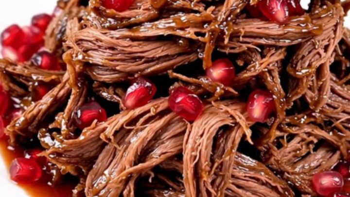 A slow cooker filled with a large beef chuck roast, sliced red onions, and pomegranate juice.