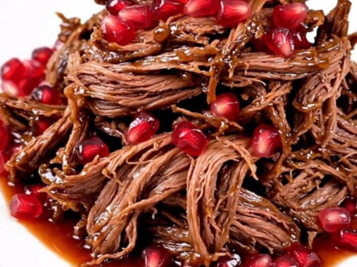 A slow cooker filled with a large beef chuck roast, sliced red onions, and pomegranate juice.