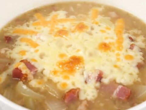 A steaming bowl of creamy onion chowder topped with melted Swiss cheese and crispy bacon bits.